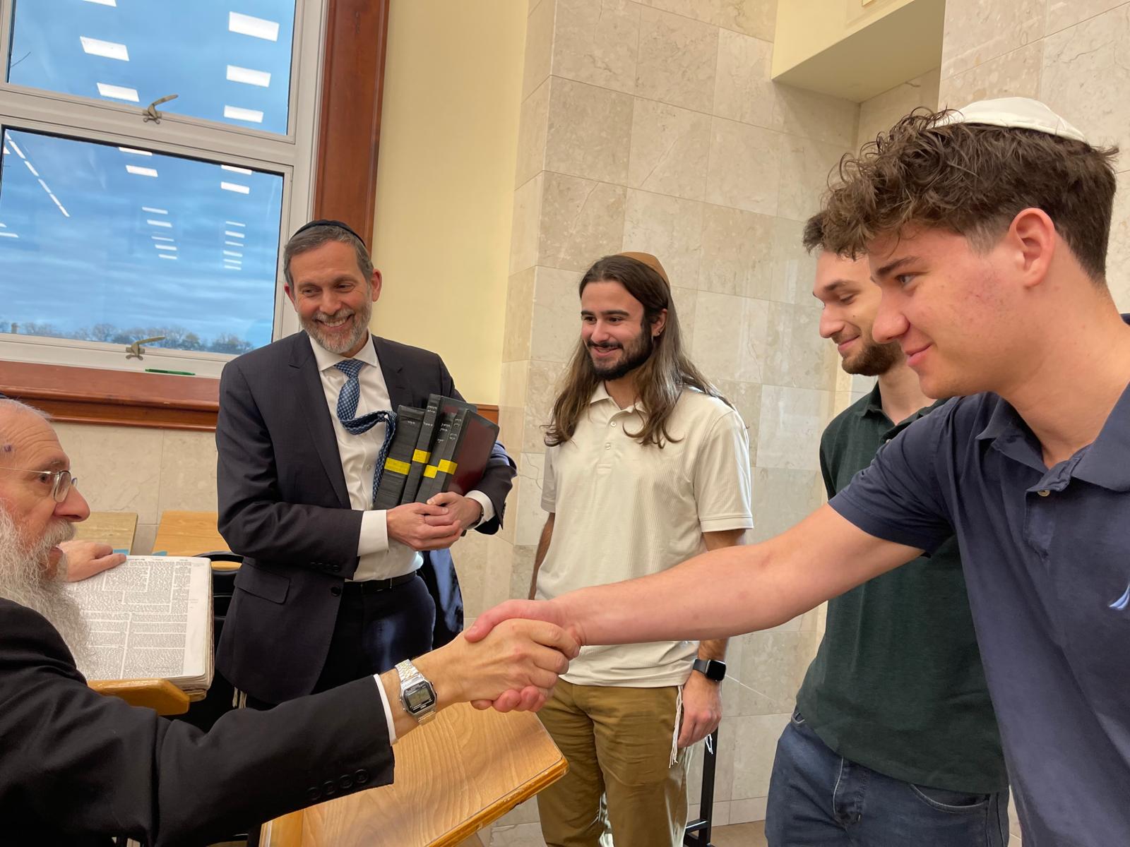 A student receiving sefarim and shaking hands with a rosh yeshiva