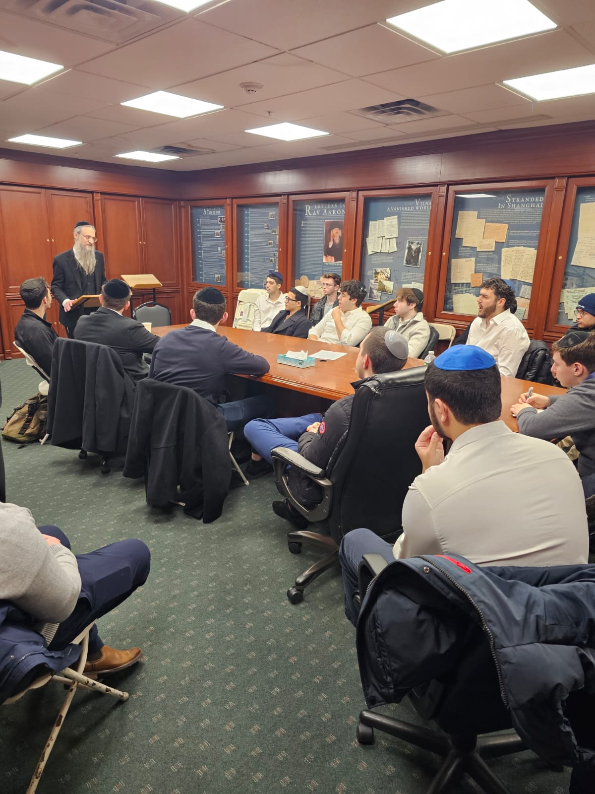 A rabbi addressing students in a wood-paneled boardroom during J³ 2025